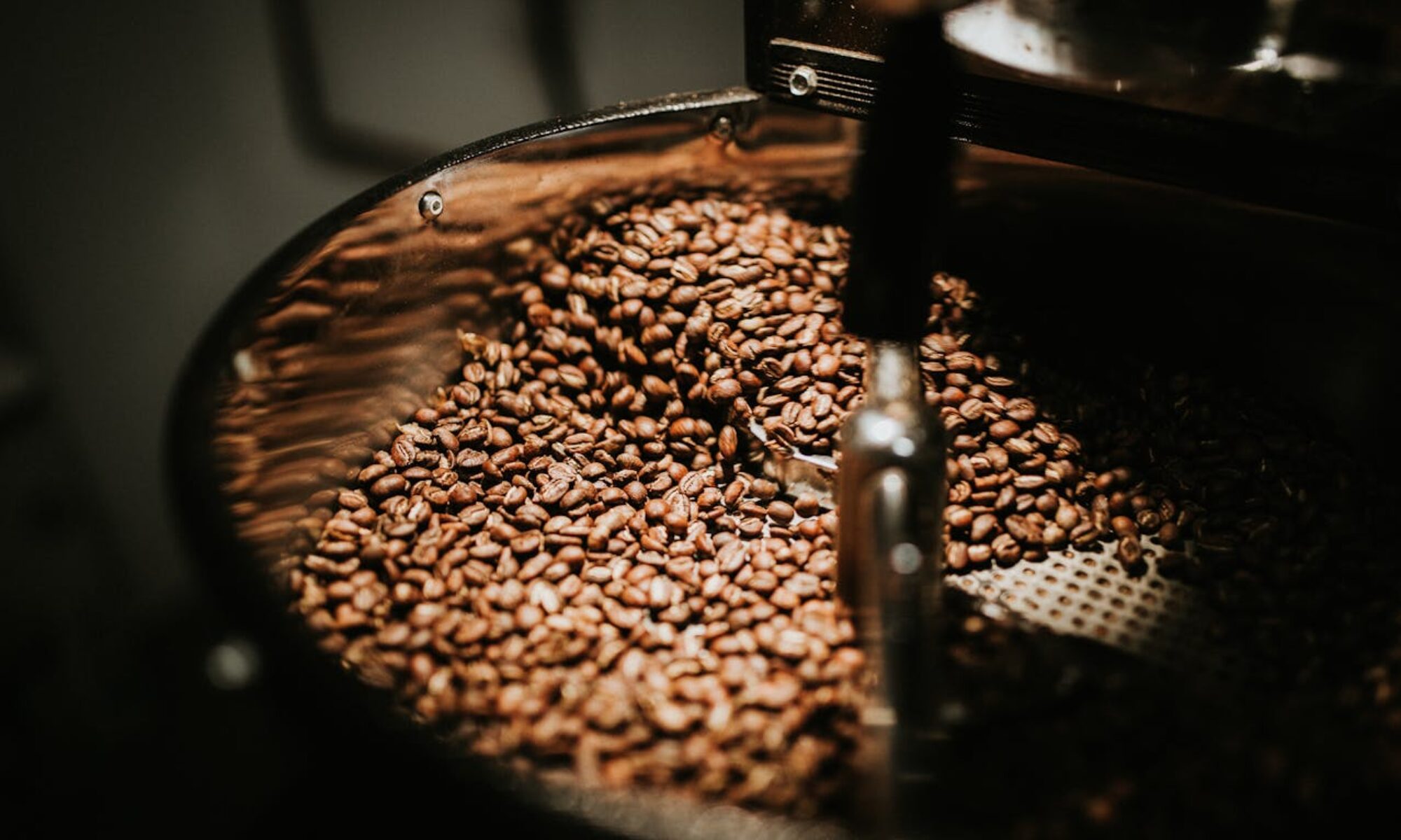 Close-up of freshly roasted coffee beans in a large industrial coffee roaster, showcasing rich textures and warm tones.